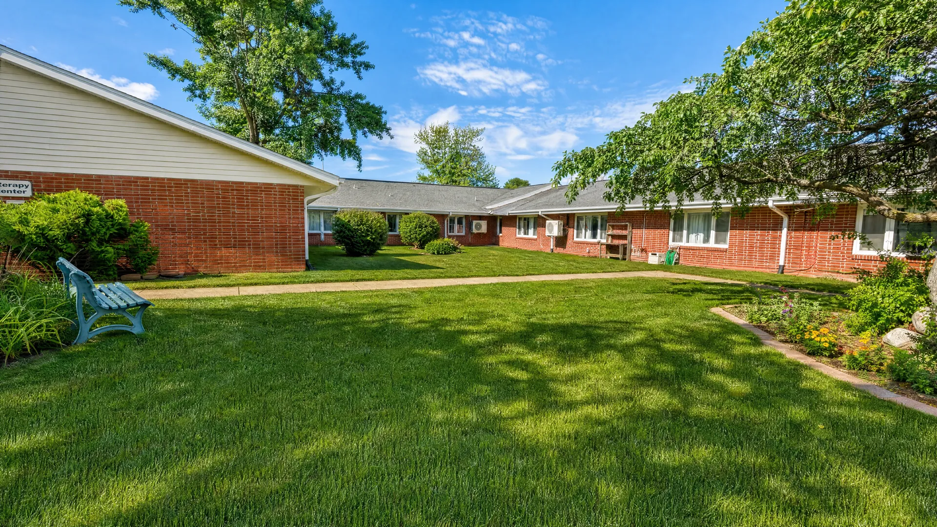 Lawn courtyard with a garden path and bench at Rehabilitation Center of Independence