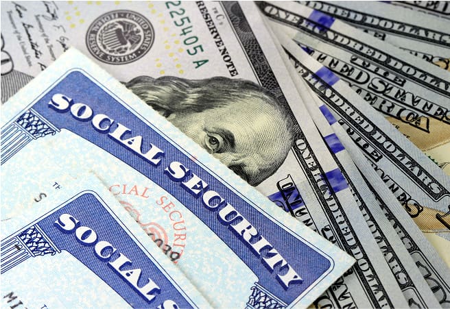 Close-up of a Social Security card and multiple U.S. dollar bills, including $20 and $100 notes, arranged on a surface.